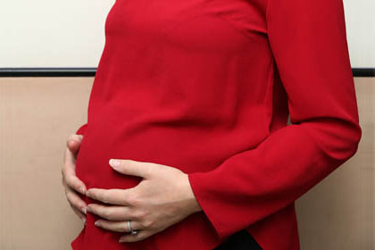 Picture showing the mid section of a pregnant woman who is wearing a red outfit and has her hands on her stomach areas. She's pregnant