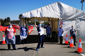 Picture of the drive-throuh testing area in front of which are five female nurses