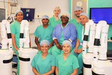 Picture of surgical staff wearing surgical gowns in a hospital operating theatre standing amongst surgical robots