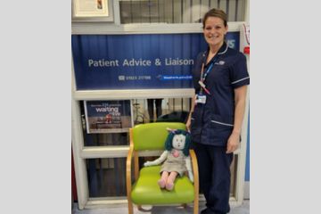 A nurse standing next to a chair on which sits a doll