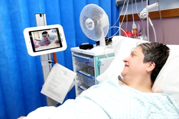 Picture of a woman in a hospital bed looking at computer screen that shows the face of a man
