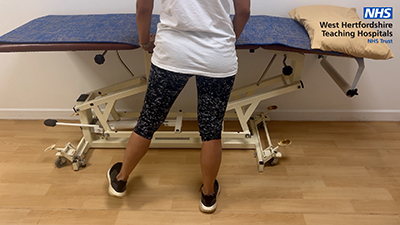 Picture of a person standing against a bed lifting their left leg