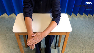 Picture of a person sitting at a table pushing down ona their right hand