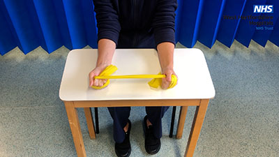 Picture of a person sitting at a table, pulling a yellow band with both hands