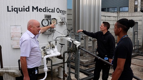 Picture of three members of staff standing next to a tank that stores liquid medical oxygen