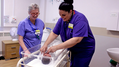 Picture of two midwives with a baby in a cot