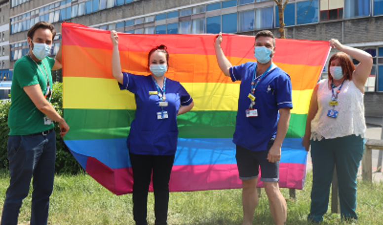Picture of four members of staff holding up a rainbow flag